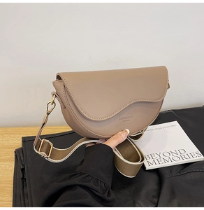 Detailed close-up of khaki saddle bag featuring contrast stitching and wide fabric strap