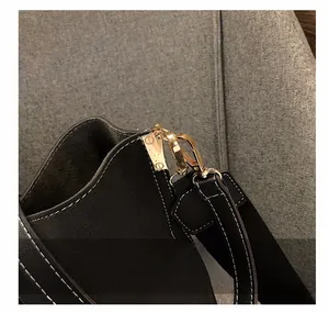 Close-up of golden metal hooks and white stitching on a black leather bucket bag