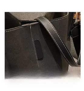 Detail of dark grey suede bucket bag showing contrast white stitching and matte texture