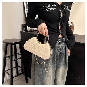 Model wearing a cream textured clutch with a gold ring handle and detachable chain strap