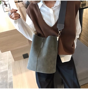 Detail of grey-green suede bucket bag with a wide fabric shoulder strap on a model