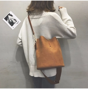 Close-up of caramel suede bucket bag with shoulder strap worn on a white sweater