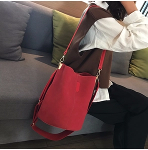 Model wearing a vibrant red suede bucket bag with adjustable wide fabric shoulder strap