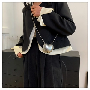 Gros plan du sac chaîne argenté en forme de cœur avec finition miroir porté par un mannequin