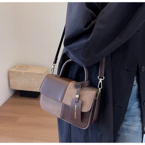 Detail of a brown two-tone crossbody bag with gold metal buckle and leather hangtag