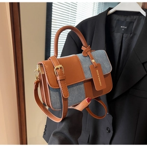Detail of contrast stitching on denim and leather handbag with gold metal hardware