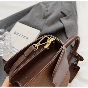 Detailed close-up of brown color-block handbag with gold hooks and mixed leather texture