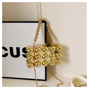 Macro detail of gold metallic evening bag featuring spherical pattern and bead handle
