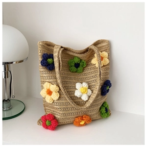 Close-up of handmade straw tote bag featuring colorful 3D crochet floral decorations