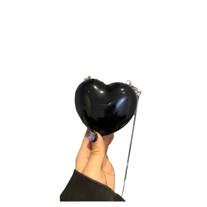 Sac à bandoulière noir verni en forme de cœur avec chaîne sur fond blanc pur