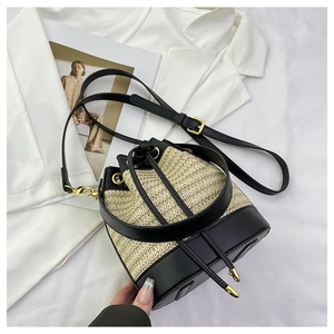 Detail of woven straw bucket bag with black leather patchwork and gold metal hardware