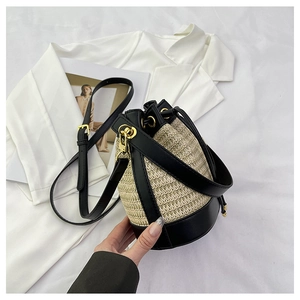 Detail view of woven straw bucket bag with black leather trim and golden hardware