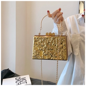 Detailed view of golden box clutch with irregular wrinkled metal texture and top handle
