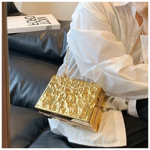 Detail of gold box clutch bag showing luxury hammered texture and metallic chain handle