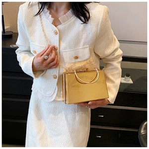 Detail of elegant gold mirror box bag with metal handle and fine chain strap