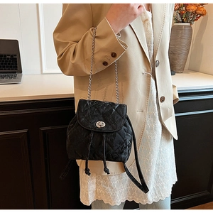 Detail of a black quilted leather backpack with silver chain straps worn by a model