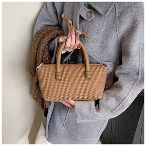 Detail shot of brown woven tote bag with cylindrical handles and metallic accents