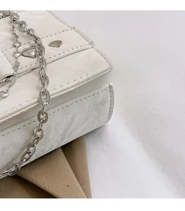 Gros plan du mini sac blanc à texture marbrée avec chaîne argentée et boucle cœur en métal