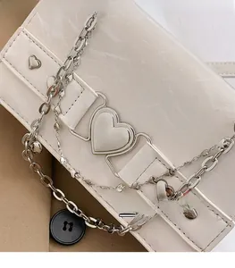 Détail du sac bandoulière en cuir crème avec fermoir coeur et chaînes décoratives