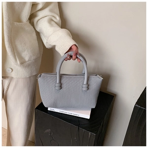 Close-up of grey tote bag with diamond quilted texture and round top handles