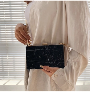 Detail of elegant black quilted clutch with gold chain strap on light clothing