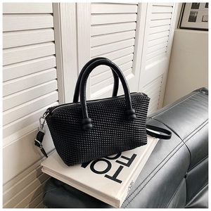 Detail of black woven textured tote bag with cylindrical handles on a fashion book