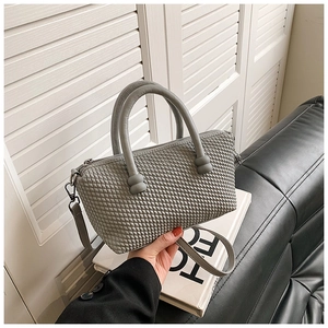 Detail shot of a grey quilted tote bag with dual handles and woven texture on a white book