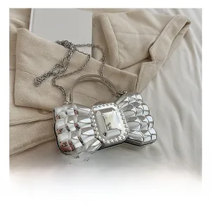 Close-up of a silver bow-shaped clutch with a large sparkling gemstone and chain strap
