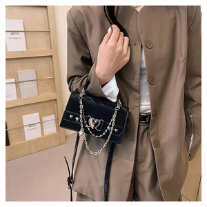 Détail du sac en cuir brillant noir avec boucle en métal coeur et bandoulière en chaîne