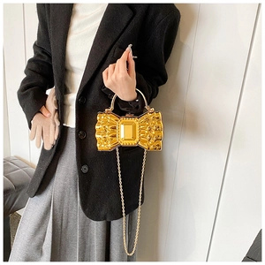 Detail of a golden bow-shaped hard shell clutch bag with a sleek metal chain strap