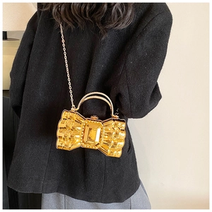 Detail of golden bow-shaped evening bag with metallic texture and large rectangular crystal