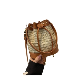 Straw drawstring bucket bag with brown leather trim and adjustable shoulder strap