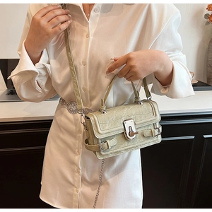 Detail of light green crocodile embossed leather bag with silver buckle and metal chain strap