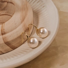 Macro shot of cream white pearl earrings with elegant gold hooks on ceramic plate