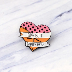 Detail of a heart-shaped enamel pin featuring BIG BUTT BIGGER HEART text on marble