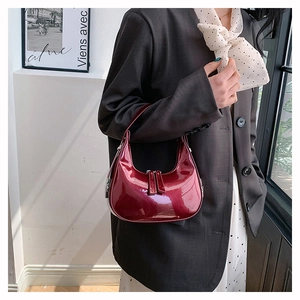 Detail van bordeauxrode laklederen halve maan tas gedragen met blazer en sjaal