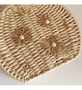 Detail of hand-woven crossbody bag with raffia flowers and faux pearl center accents