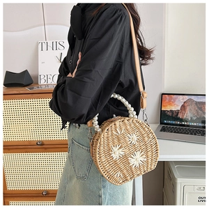 Detail of round straw bag featuring pearl handles and floral pearl ornaments with strap