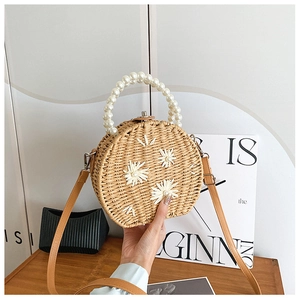 Detail of round straw bag with daisy embroidery, pearl handle and leather shoulder strap