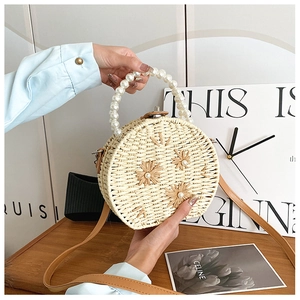 Detail of round woven straw bag with pearl handle and 3D floral embroidery accents