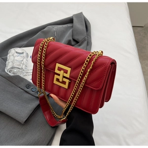 Detail of red quilted crossbody bag with golden geometric clasp and metal chain strap