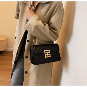 Detail of black quilted leather crossbody bag with gold geometric clasp on a model
