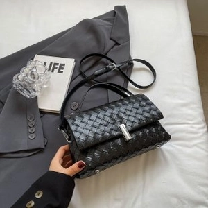 Detail of black woven leather crossbody bag with silver metal lock on a white bed sheet