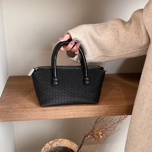 Elegant black woven tote bag with top handles shown in a minimalist lifestyle setting