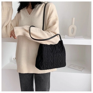 Close-up of black cable-knit texture and slim leather strap on a minimalist shoulder bag