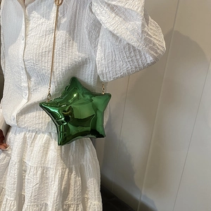 Borsa a tracolla a stella verde metallizzato con catena dorata su sfondo camicia bianca