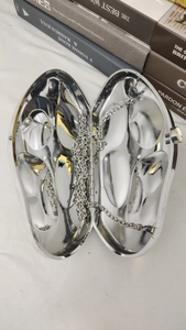 Top view of an open oval silver mirror clutch bag with a metallic chain and snap closure
