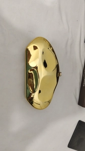 Close-up of a gold asymmetric metallic clutch bag with a high-shine mirror finish surface