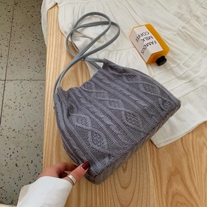 Minimalist grey knit shoulder bag with cable pattern on a textured wooden background