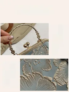 Close-up of golden floral embroidery on light blue satin evening bag with metal handle